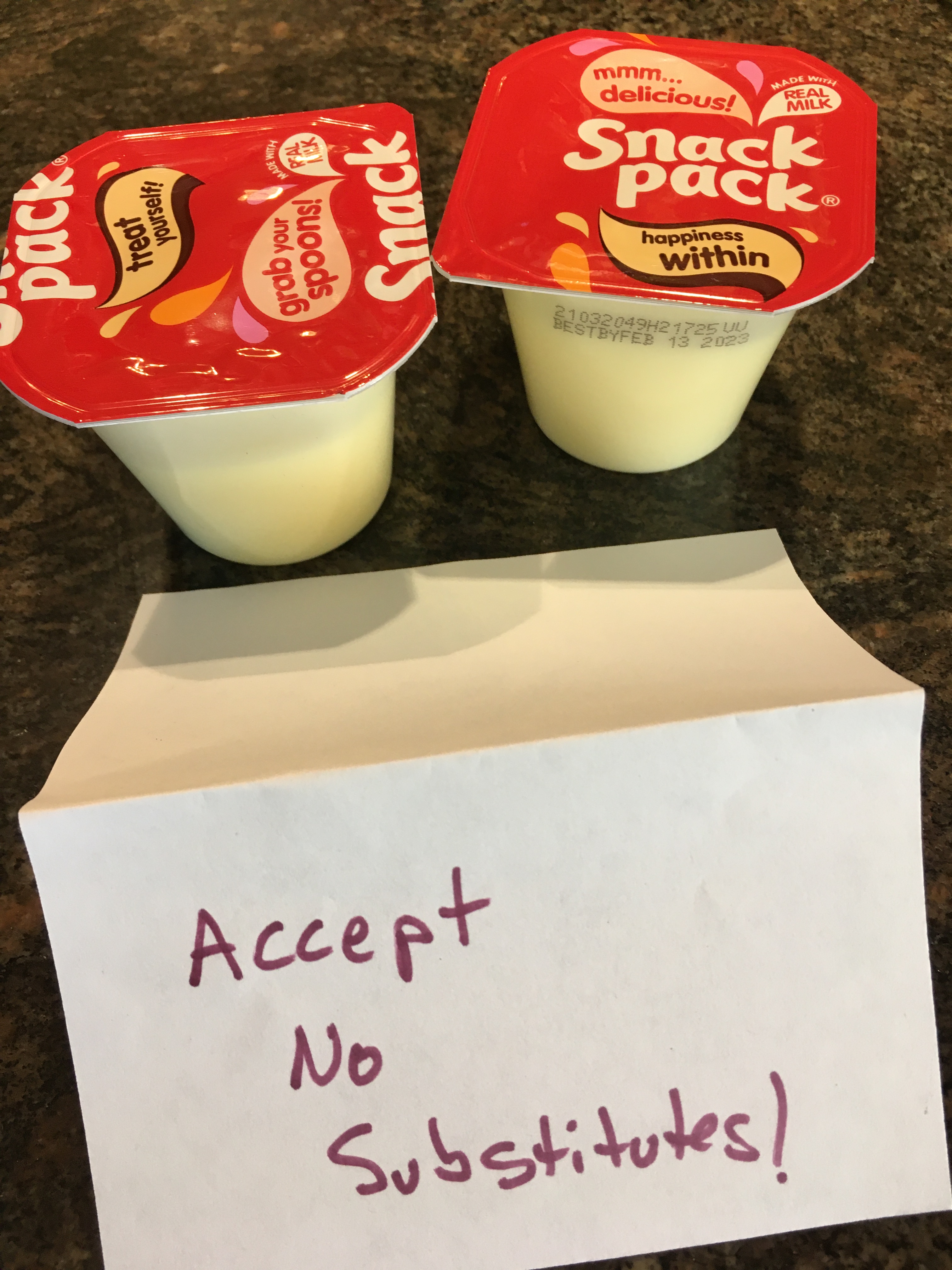 Photo of two individual serving Snack Pack vanilla pudding cups, with a hand-made sign in front of them reading "Accept No Substitutes!"